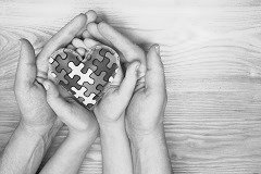 Zwei Kinderhände liegen in zwei Händen eines Erwachsenen und halten Puzzleteile